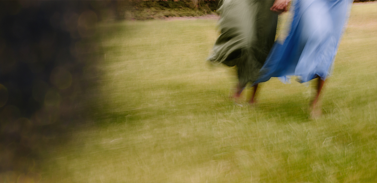 Two people in flowing dresses walking on grass