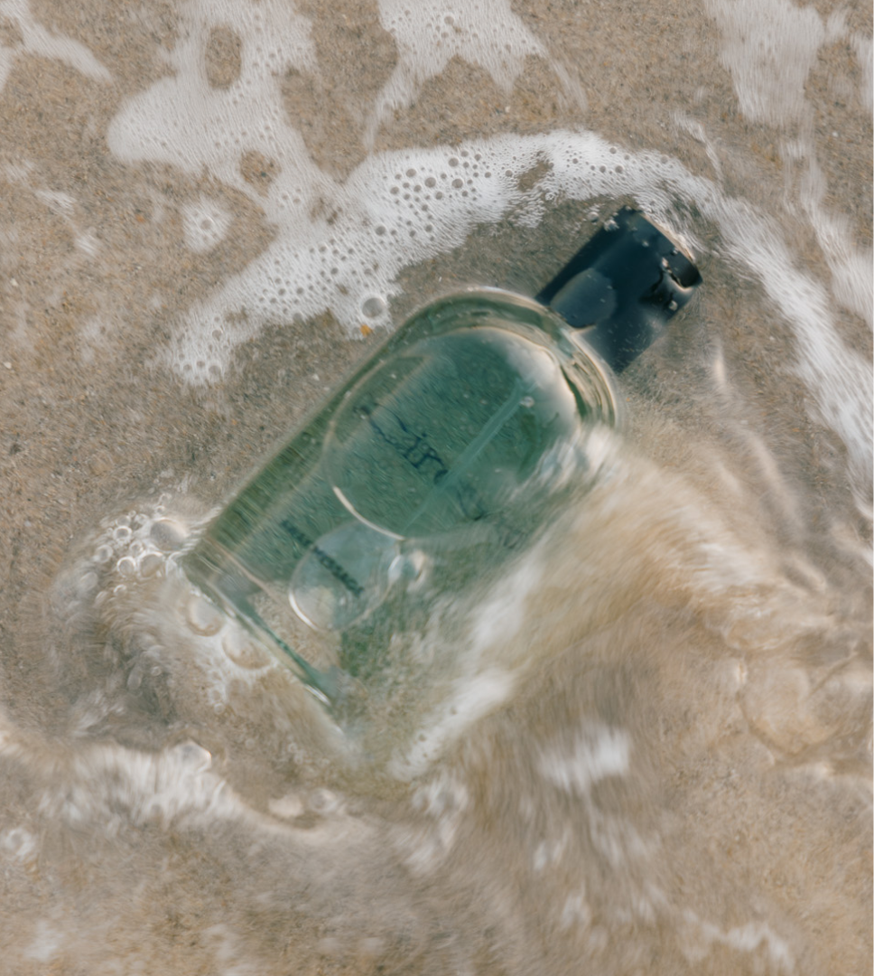 Aerial view of a Cirqadian fragrance bottle washed by ocean surf and foam on the sand
