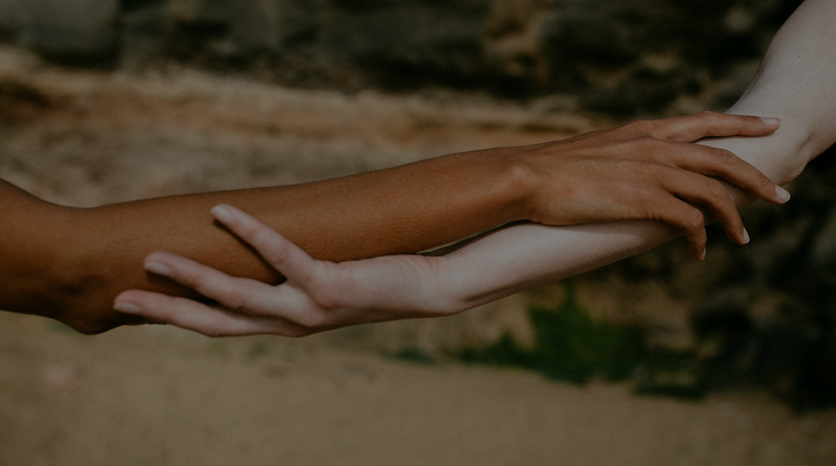 Two human arms and hands touching in a close-up outdoor scene, with a blurred natural background.