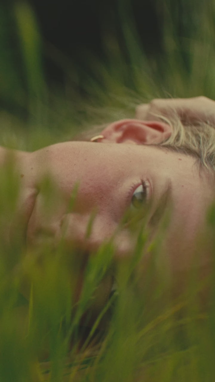 Close-up of a person's face resting in green grass with a calm expression, video thumbnail